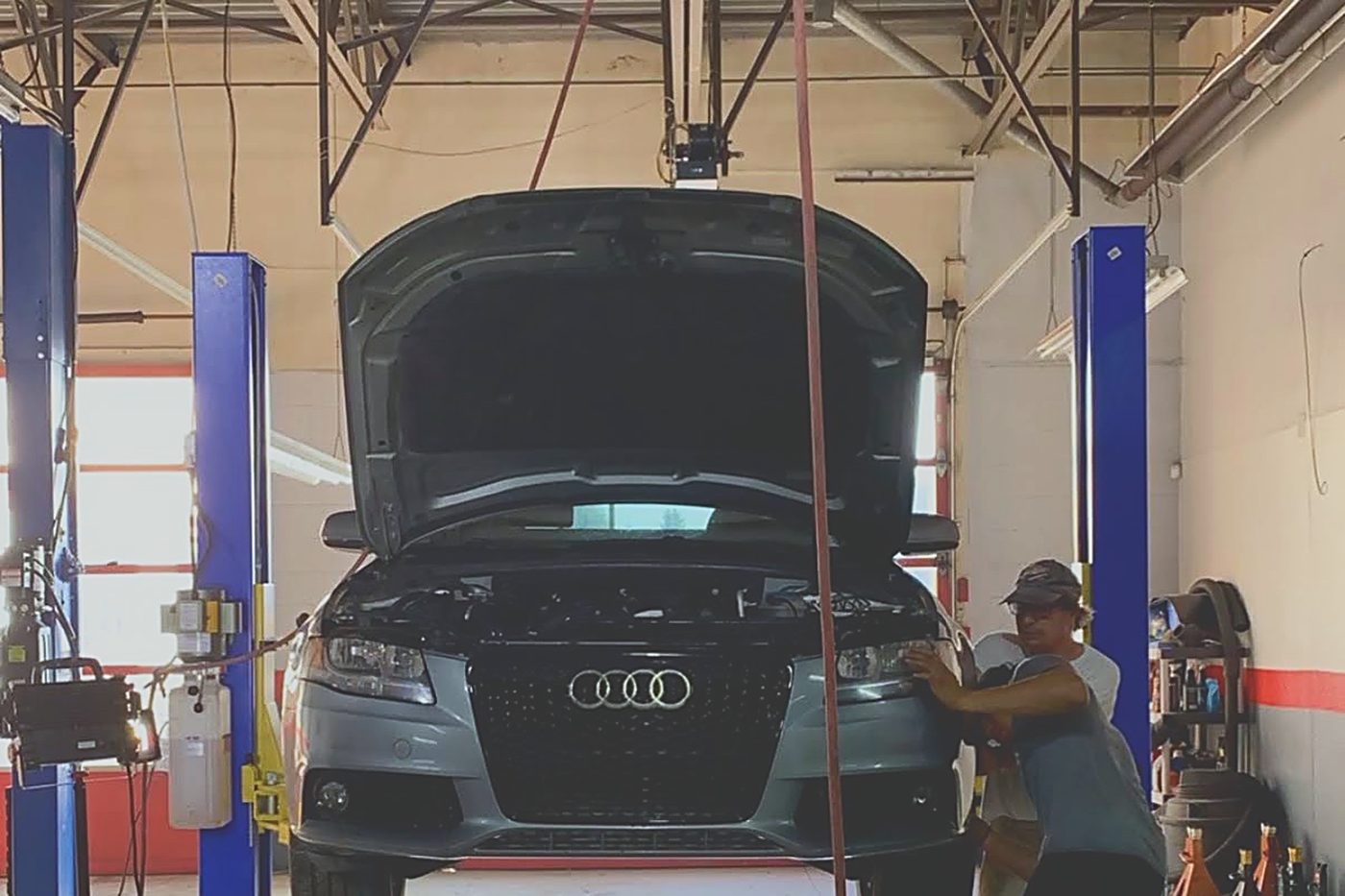 A customer's Audi raised on one of our two-post lifts with the hood up, someone working at the front of it.