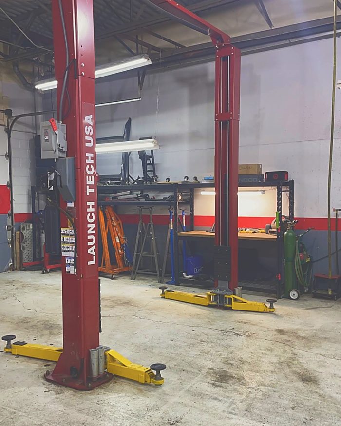 A two-post lift standing empty, with the workbench, jack stands and shop tools behind it.